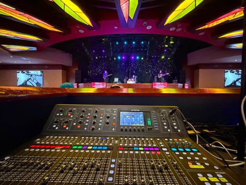Digital mixing console in front of a showroom stage with ceiling lighting