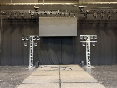 Stage with a truss lighting rig, two truss trees with fixtures and an LED video wall panel mounted on black drape