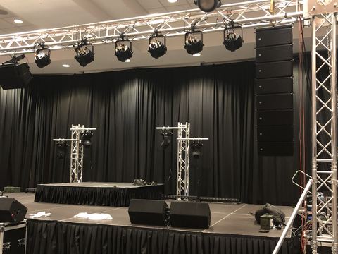 Skirted stage decks with black drape behind, a lighting truss with fixtures overhead, truss towers and two small truss totems on stage